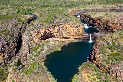 Aerial view of the multi-tiered Mitchell Falls cascading through rugged sandstone gorges into large emerald pools.