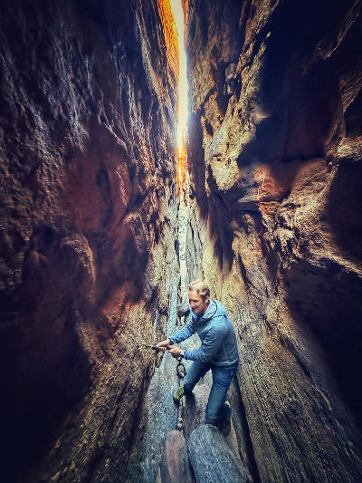 Hiker navigating a narrow sandstone passage inside Wolfberg Cracks in the Cederberg Wilderness Area, Western Cape, South Africa.