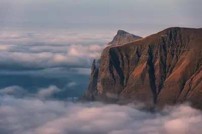 Trøllkonufingur sea stack, known as the Witch’s Finger, standing beside steep coastal cliffs at sunrise above cloud-covered Atlantic waters on Vágar Island, Faroe Islands.