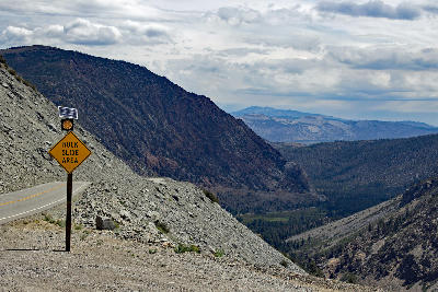 Tioga Pass Road with rock slide warning sign along steep mountain slope in the eastern Sierra Nevada near Yosemite National Park.