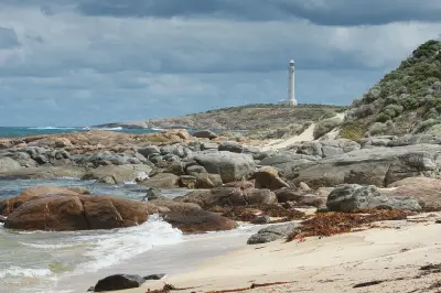 Cape Leeuwin Lighthouse above a rugged granite shoreline, sandy beach and breaking waves in Western Australia.