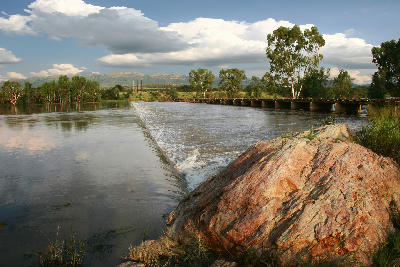 Vaal River flowing over the Schoemansdrif weir beside a bridge crossing within the Vredefort Dome landscape.