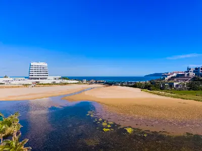 View of Lookout Beach and the estuary mouth in Plettenberg Bay, featuring sandy flats, tidal waters, the Beacon Island Hotel and the Indian Ocean beyond.