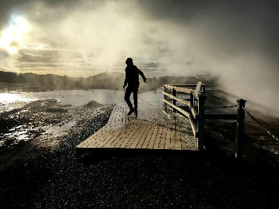 Silhouette of a person walking on a wooden boardwalk through steam at Gunnuhver geothermal field on the Reykjanes Peninsula, Iceland.