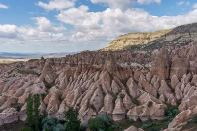 Panoramic view of Rose Valley in Cappadocia, Turkey, with pink volcanic ridges, fairy chimneys and layered cliffs beneath a cloud-filled sky.