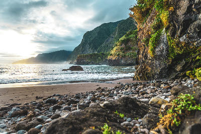 Waterfall cascading from coastal cliffs onto the black sand of Seixal Beach on Madeira Island, Portugal.