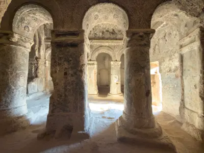 Interior of a rock-cut church at Göreme Open Air Museum with stone columns, vaulted ceilings and faded Byzantine frescoes carved into the volcanic rock of Cappadocia, Turkey.