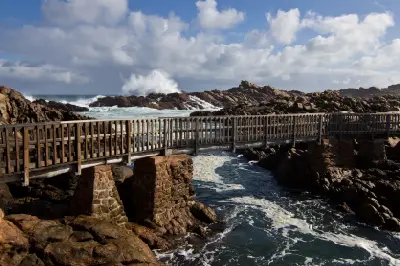 Wooden footbridge crossing the rocky ocean channel at Canal Rocks near Yallingup, Western Australia, with waves breaking over granite reefs.