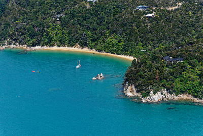Aerial view of Anchorage Bay with golden beach, kayakers and anchored sailboat in Abel Tasman National Park, New Zealand.