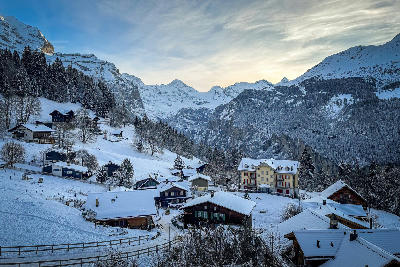 Snow-covered chalets in Wengen overlooking Lauterbrunnen Valley, with forested slopes and alpine peaks under winter light, Switzerland.