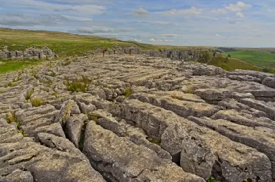 Fractured limestone pavement with deep natural fissures and walkers above the cliffs of Malham Cove in North Yorkshire, England.