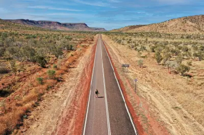 Long road stretches through dry savanna toward rugged red escarpments near El Questro in the East Kimberley.