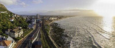 Aerial view of Muizenberg Beach on False Bay with railway, coastal road, and long sandy shoreline at sunrise in Cape Town, South Africa.