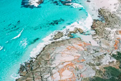 Aerial view of turquoise ocean and orange-lichen granite rocks along the Bay of Fires, Tasmania.