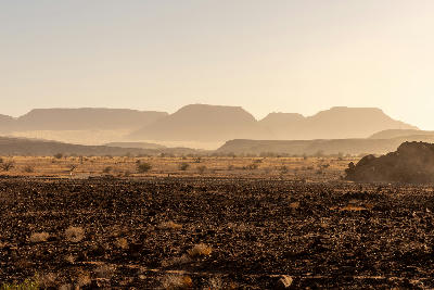 Arid plains and distant granite mesas near Spitzkoppe in Namibia under dusty golden evening light.