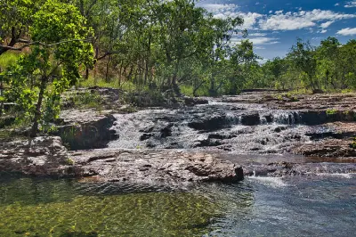 Shallow cascades flowing across rocky ledges into a clear pool, surrounded by tropical woodland in Litchfield National Park, Northern Territory, Australia.