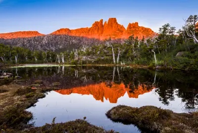 Mount Acropolis glowing in warm evening light and reflected in an alpine tarn in Tasmania’s Cradle Mountain–Lake St Clair National Park.