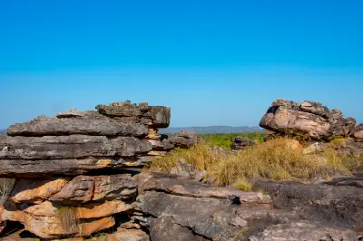 Layered sandstone outcrops rise above dry grasses on the rocky Ubirr landscape, displaying the weathered formations characteristic of Kakadu's Arnhem Land escarpment.