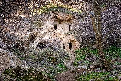Ancient rock-cut dwellings surrounded by trees along the floor of Ihlara Valley, Turkey.