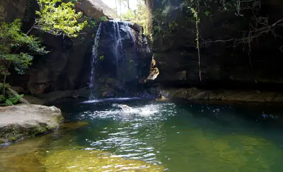 Swimmer beneath a shaded canyon waterfall in Isalo National Park, Madagascar