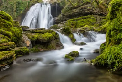 Long-exposure photograph of Janet's Foss waterfall flowing over moss-covered limestone rocks into a woodland pool in North Yorkshire, England.