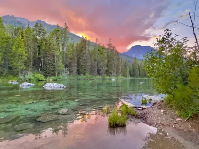 Clear water of String Lake with rocks and forest reflected under pink and purple sunset in Grand Teton National Park, Wyoming, USA.