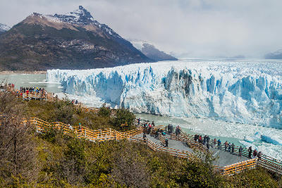 Tourists standing on wooden viewing platforms overlooking Perito Moreno Glacier ice wall in Patagonia, Argentina.