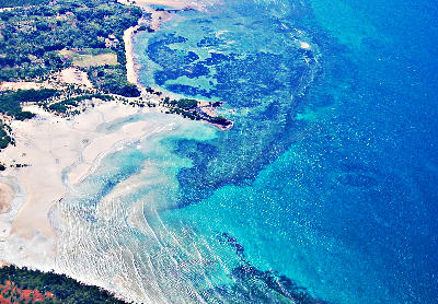 Aerial coastal landscape near Nosy Be in Madagascar showing turquoise reef waters, tidal sandbars, and tropical shoreline patterns.