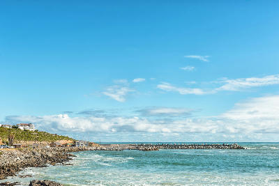 Yzerfontein Harbour with rock breakwaters extending into the Atlantic Ocean, viewed from the rocky shoreline beneath coastal hills and homes.