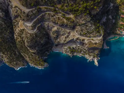 Aerial view of the winding road on Babadağ Mountain above the turquoise Mediterranean coast near Fethiye, Turkey.