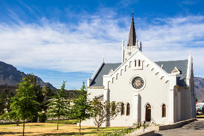Historic white Dutch Reformed church in Barrydale with mountain scenery and blue sky in the Western Cape, South Africa.