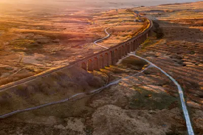 Aerial view of Ribblehead Viaduct in golden morning light, with its long stone arches and shadows extending across Batty Moss in the Yorkshire Dales.