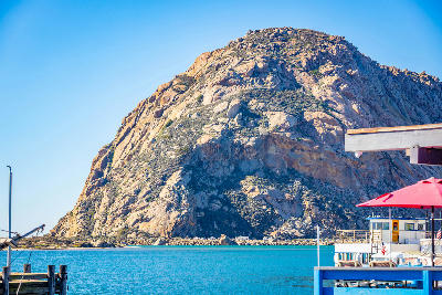 Morro Rock volcanic plug in Morro Bay California with blue harbor water and coastal buildings in foreground