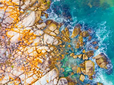 Aerial view of orange lichen-covered granite rocks and turquoise ocean water near The Gardens, Bay of Fires, Tasmania.