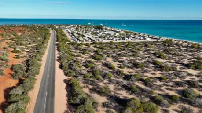 Coastal road, accommodation and shoreline at Monkey Mia beside the blue waters of Shark Bay.