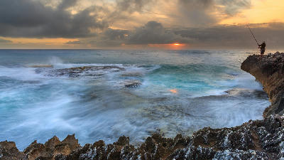 Fisherman on rocky cliffs above turbulent ocean waves near Arniston on the Western Cape coast of South Africa at sunrise.