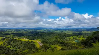 Panoramic view of green farmland, winding roads and forested hills beneath a cloudy sky in the Atherton Tablelands, Queensland.