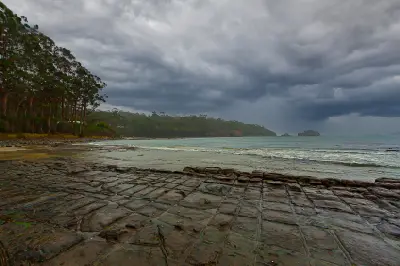 Tessellated Pavement rock formations beneath dark storm clouds on the Tasman Peninsula, Tasmania.