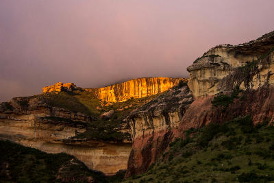 Golden sandstone cliffs illuminated by evening sunlight in Golden Gate Highlands National Park, with layered rock formations and misty mountain slopes in the eastern Free State, South Africa.