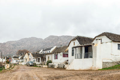 Traditional whitewashed cottages with thatched roofs along a dirt road in Wupperthal, framed by the rugged sandstone mountains of the northern Cederberg.