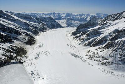 Aerial view of the Aletsch Glacier flowing between snow-covered alpine peaks in the Swiss Alps.