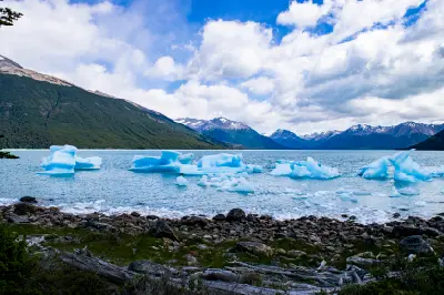 Icebergs floating on Lago Argentino with mountains and shoreline in Patagonia, Argentina.