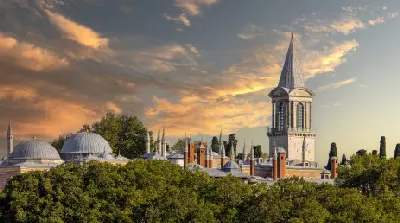 Topkapı Palace in Istanbul at sunset, showing Ottoman domes and the Tower of Justice beneath dramatic golden clouds.