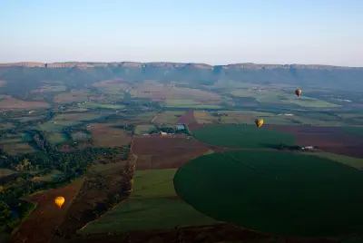 Hot-air balloons floating above farmland beneath the Magaliesberg escarpment in North West Province, South Africa.