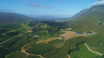 Aerial view including Creation Wines within the Hemel-en-Aarde Valley, showing vineyards, mountain slopes, reservoirs, and layered agricultural landscapes near Hermanus, South Africa.