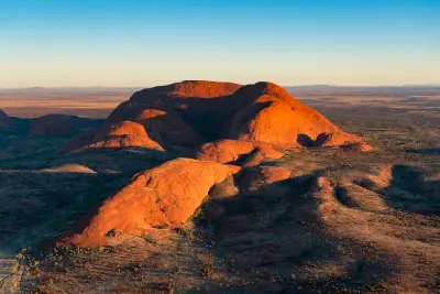 Aerial view of Kata Tjuta's rounded sandstone domes illuminated by low evening light above the Central Australian desert.
