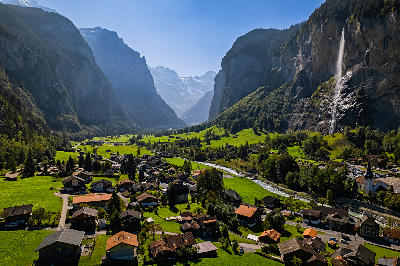 Elevated view over Lauterbrunnen Valley with village houses, river, green meadows, and Staubbach Falls descending from steep cliffs, Switzerland.