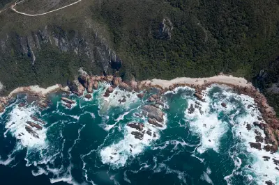 Aerial view of rocky shoreline, forested cliffs and surf along the Tsitsikamma Coast in South Africa.