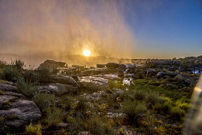 Sunrise shining through waterfall spray above the granite plateau and boardwalks at Augrabies Falls.