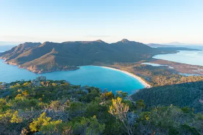 Elevated view over the turquoise waters and sweeping white-sand beach of Wineglass Bay beneath rugged mountains in Freycinet National Park, Tasmania.